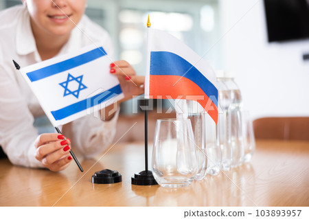 Unrecognizable girl sets midget flags of Russia and Israel before international negotiations 103893957