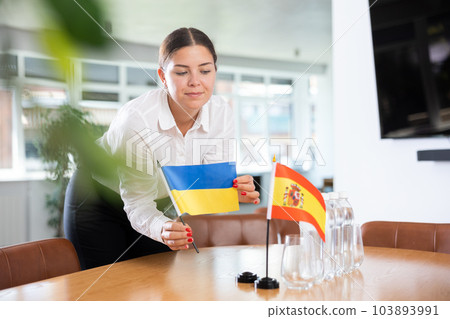Young woman puts flags of Ukraine and Spain on table in office Young woman puts flags of Ukraine and Spain on table in office 103893991