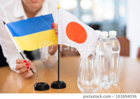 Little flag of Japan on table and flag of Ukraine put next to it by young woman Little flag of Japan on table and flag of Ukraine put next to it by young woman 103894036