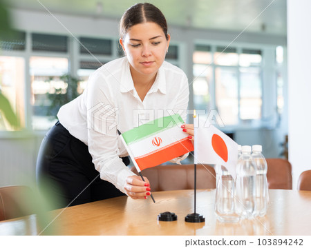 Female office coordinator placing flags of Iran and Japan on table before negotiations 103894242