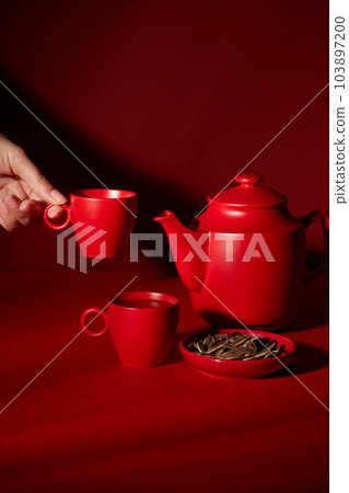 Against the red background, red tea cup set decorated with plate of sunflower seed. Female hand is pick up a small cup. Minimal style, advertising photo for product Against the red background, red tea cup set decorated with plate of sunflower seed. Female hand is pick up a small cup. Minimal style, advertising photo for product 103897200