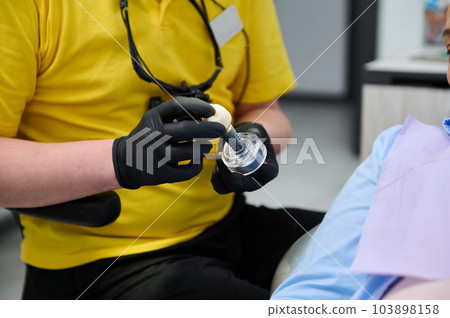 Close-up doctor dentist orthodontist holding a sample of veneer dental implant. Dental practice. Aesthetic dentistry. Denture. Dental prosthesis. Healthcare and medicine Close-up doctor dentist orthodontist holding a sample of veneer dental implant. Dental practice. Aesthetic dentistry. Denture. Dental prosthesis. Healthcare and medicine 103898158