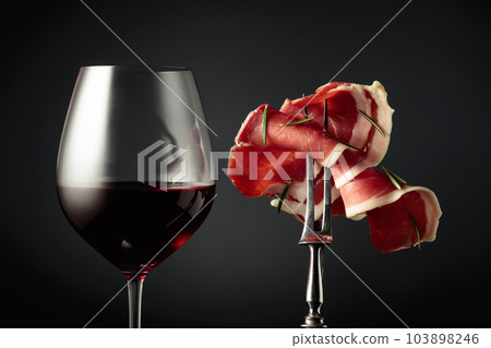 Glass of red wine and sliced prosciutto with rosemary. 103898246