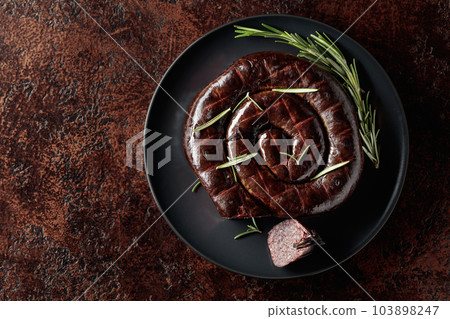 Black pudding or blood sausage with rosemary on a black plate. 103898247