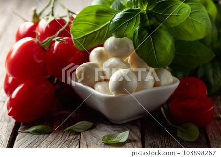 Mozzarella cheese with basil and tomatoes on an old wooden table. 103898267