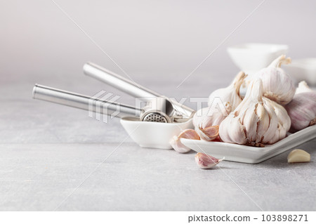 Garlic and garlic press on a grey table. 103898271