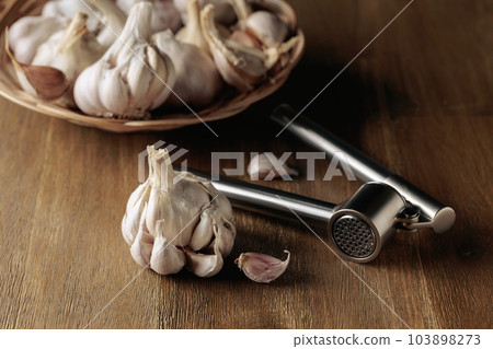 Garlic bulbs and garlic press on a wooden table. Garlic bulbs and garlic press on a wooden table. 103898273