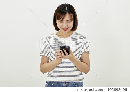 Smiling Asian woman using a smartphone, standing against texting on a mobile phone on white background, people and technology concept 103898496