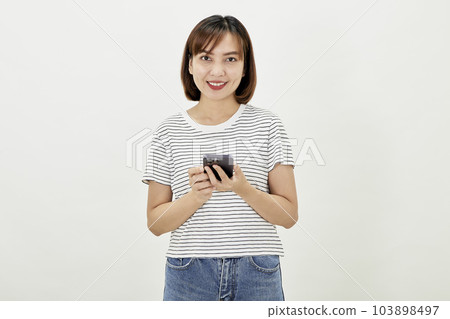 Smiling Asian woman using a smartphone, standing against texting on a mobile phone on white background, people and technology concept Smiling Asian woman using a smartphone, standing against texting on a mobile phone on white background, people and technology concept 103898497
