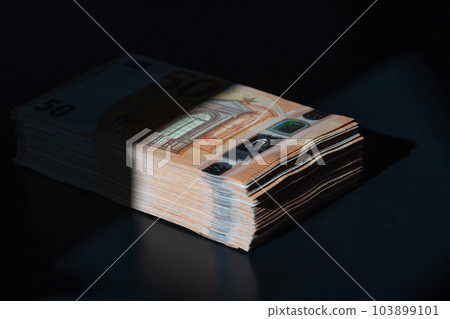 A big wad of money half in the shade on the black table. Euro money banknotes in shadow. 50 euro pack. The concept of the shadow economy. A big wad of money half in the shade on the black table. Euro money banknotes in shadow. 50 euro pack. The concept of the shadow economy. 103899101