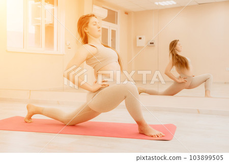 Young sporty woman, fitness instructor in sportswear doing stretching and pilates on yoga mat in the studio with mirror. Female fitness yoga routine concept. Healthy lifestyle and harmony. 103899505