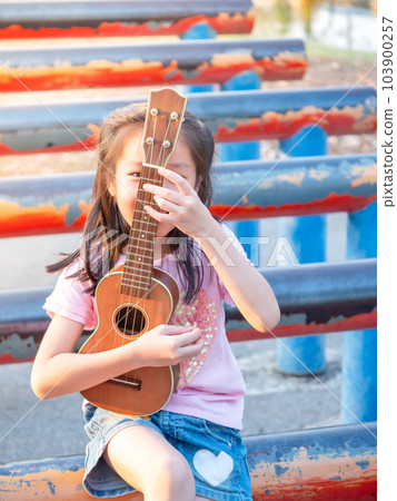 Little asian child girl play the ukulele, in the garden on the Steel pipe, practice to play Little asian child girl play the ukulele, in the garden on the Steel pipe, practice to play 103900257