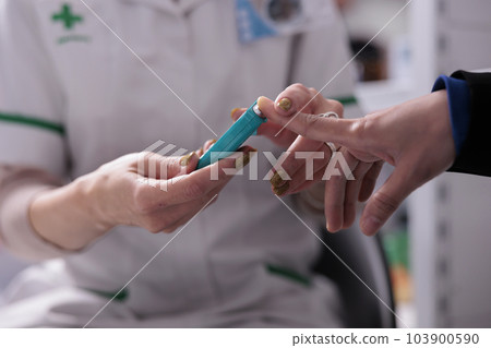Woman measuring blood sugar level for diabetes screening in apothecary. Pharmacy employee using glucometer in pharmaceutical store, pressing client finger to medical device close up 103900590