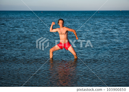 Slim guy posing in red swimwear in sea water 103900850