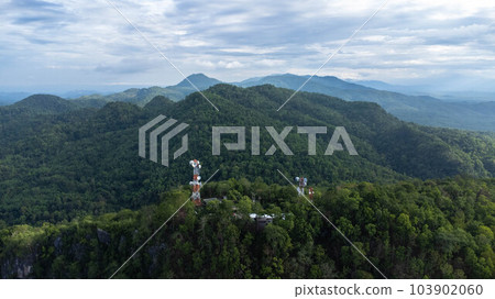 Communication tower, radio tower, telecommunication tower or transmission tower in the forest on the mountain with clouds and blue sky background. Communication tower, radio tower, telecommunication tower or transmission tower in the forest on the mountain with clouds and blue sky background. 103902060