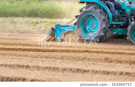 Tractor cultivating land with a rotary tiller in farm. Tractor cultivating land with a rotary tiller in farm. 103904757