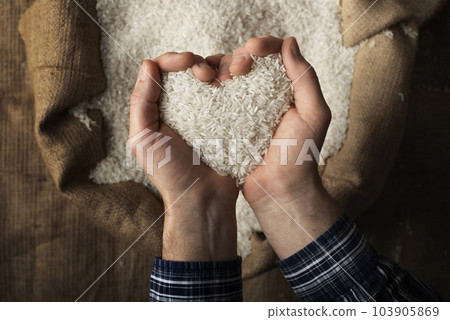 Human hands in shape of heart holding handful of rice over burlap sack 103905869