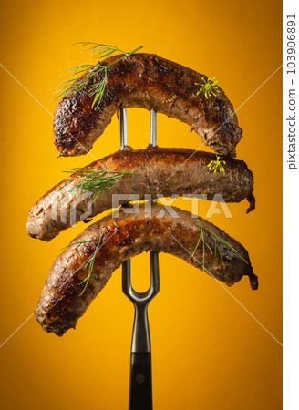 Grilled sausages with veal on a fork. Delicious lunch concept for hotel on yellow background Grilled sausages with veal on a fork. Delicious lunch concept for hotel on yellow background 103906891