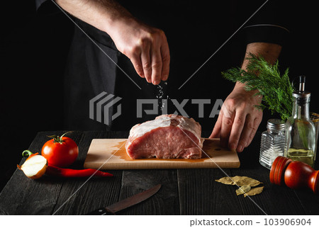 The chef sprinkles the meat with salt. Preparing meat before baking. Working environment in the kitchen of restaurant or cafe 103906904