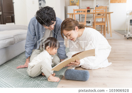 A young couple reading a picture book to an infant 103906928