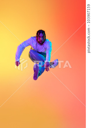 Young bearded man with dreads in casual clothes dancing breakdance against gradient orange yellow studio background in neon light Young bearded man with dreads in casual clothes dancing breakdance against gradient orange yellow studio background in neon light 103907159