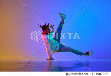 Young handsome guy in casual clothes and dreads dancing breakdance against gradient multicolored studio background in neon light 103907165