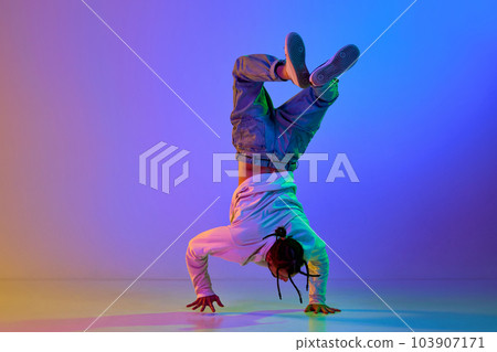 Flexible young man, contemp dancer performing breakdance, hip-hop against gradient multicolored studio background in neon light 103907171