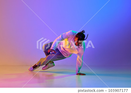 Young guy with dreads, in casual clothes dancing hip-hop, breakdance against gradient multicolored studio background in neon light 103907177