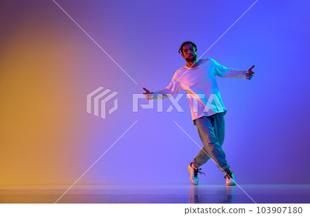 Dance show. Young guy dancing contemp, breakdance and hip-hop against gradient multicolored studio background in neon light 103907180