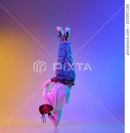 Young sportive guy with dreads hairstyle dancing hip-hop, breakdance against gradient multicolored studio background in neon light Young sportive guy with dreads hairstyle dancing hip-hop, breakdance against gradient multicolored studio background in neon light 103907188
