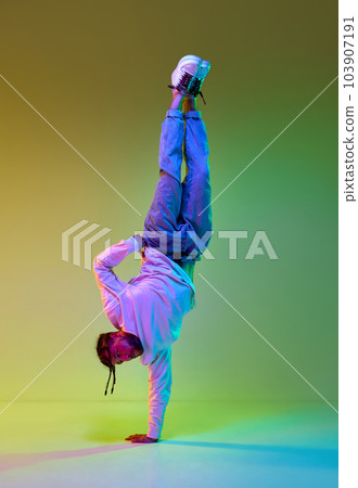 Young man with dreads hairstyle dancing hip-hop, breakdance against gradient yellow green studio background in neon light Young man with dreads hairstyle dancing hip-hop, breakdance against gradient yellow green studio background in neon light 103907191