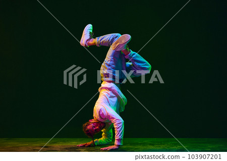 Young artistic man in sportive clothes dancing breakdance, hip-hop, street dance against black studio background in neon light 103907201
