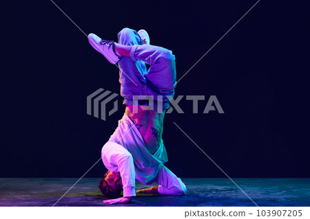 Artistic, sportive young man in sprotive clothes dancing breakdance, hip-hop against black studio background in neon light 103907205
