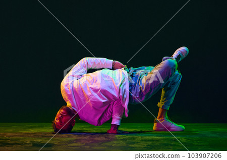 Flexibility. Young man in sport style clothes dancing hip-hop, breakdance against black studio background in neon light 103907206