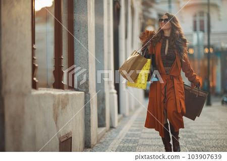 smiling modern woman in orange trench coat with shopping bags smiling modern woman in orange trench coat with shopping bags 103907639