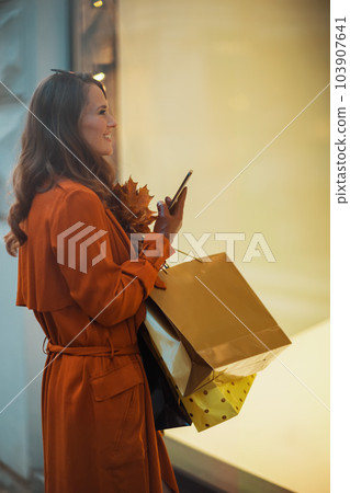 happy elegant woman in orange trench coat with shopping bags happy elegant woman in orange trench coat with shopping bags 103907641