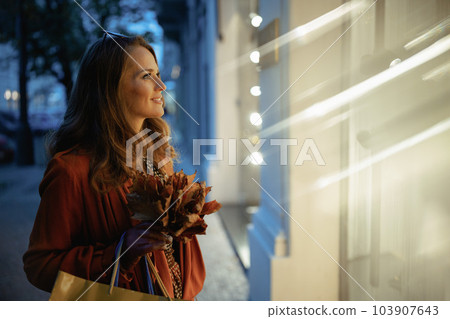 smiling young woman in orange trench coat with shopping bags 103907643