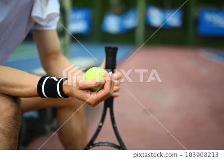 Select focus on hands of male tennis player holding ball racket sitting on the bench at tennis court 103908213