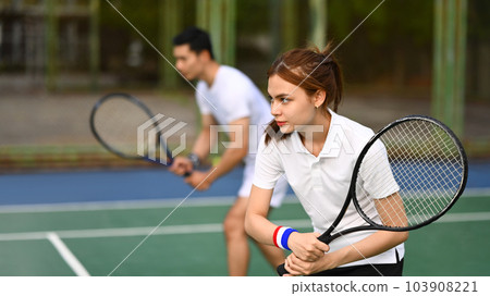 Focused female athlete with a racket waiting to receive ball during match at outdoor court 103908221