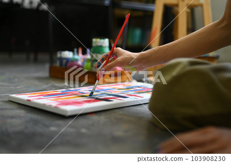 Cropped shot of artist sitting on floor in art studio and painting on canvas with watercolors 103908230