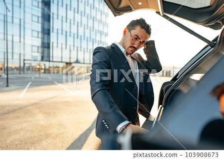 Successful businessman taking luggage from the car trunk Successful businessman taking luggage from the car trunk 103908673