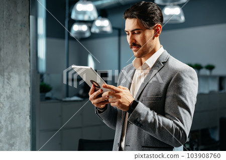Young successful businessman working on digital tablet while standing in office 103908760