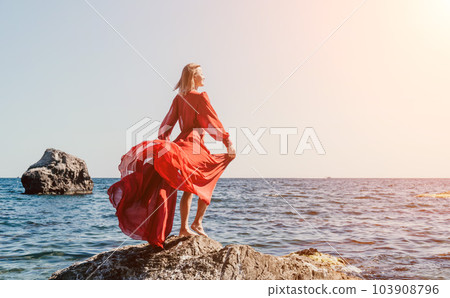 Woman travel sea. Happy tourist in long red dress enjoy taking picture outdoors for memories. Woman traveler posing on beach at sea surrounded by volcanic mountains, sharing travel adventure journey 103908796