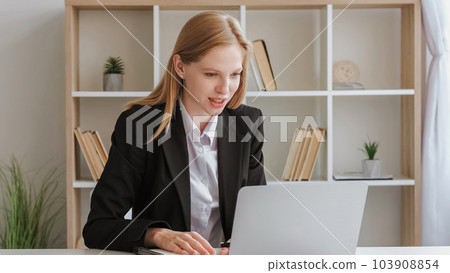 Video call. Online interview. Business communication. Confident smiling young blond woman in suit sitting at table talking to laptop at white office. Video call. Online interview. Business communication. Confident smiling young blond woman in suit sitting at table talking to laptop at white office. 103908854