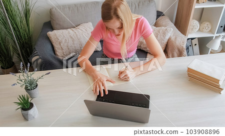 Online education. Student homework. Prepare professional. Concentrated young blond girl write notes work with laptop at table at home. 103908896