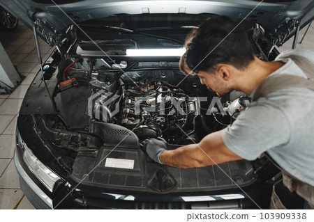 Young male mechanic examining engine under hood of car at the repair garage Young male mechanic examining engine under hood of car at the repair garage 103909338