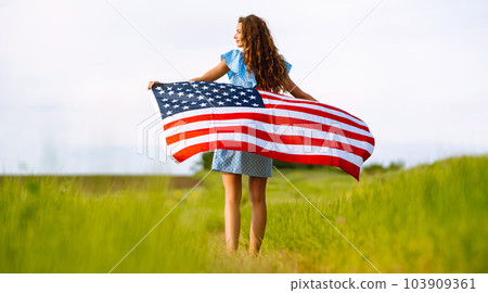 Young woman with american USA flag on blooming meadow. Independence Day, 4th July. 103909361
