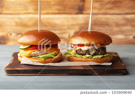 Two burgers on wooden board on gray table 103909690