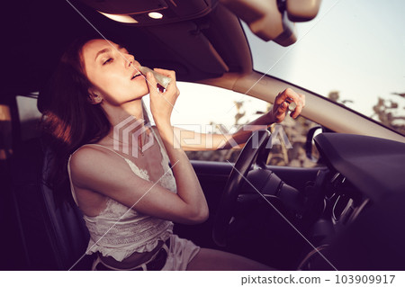 Beautiful young caucasian woman painting lips on the front seat of her car 103909917