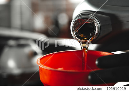 Close up of car service worker pouring new oil into car engine 103910019